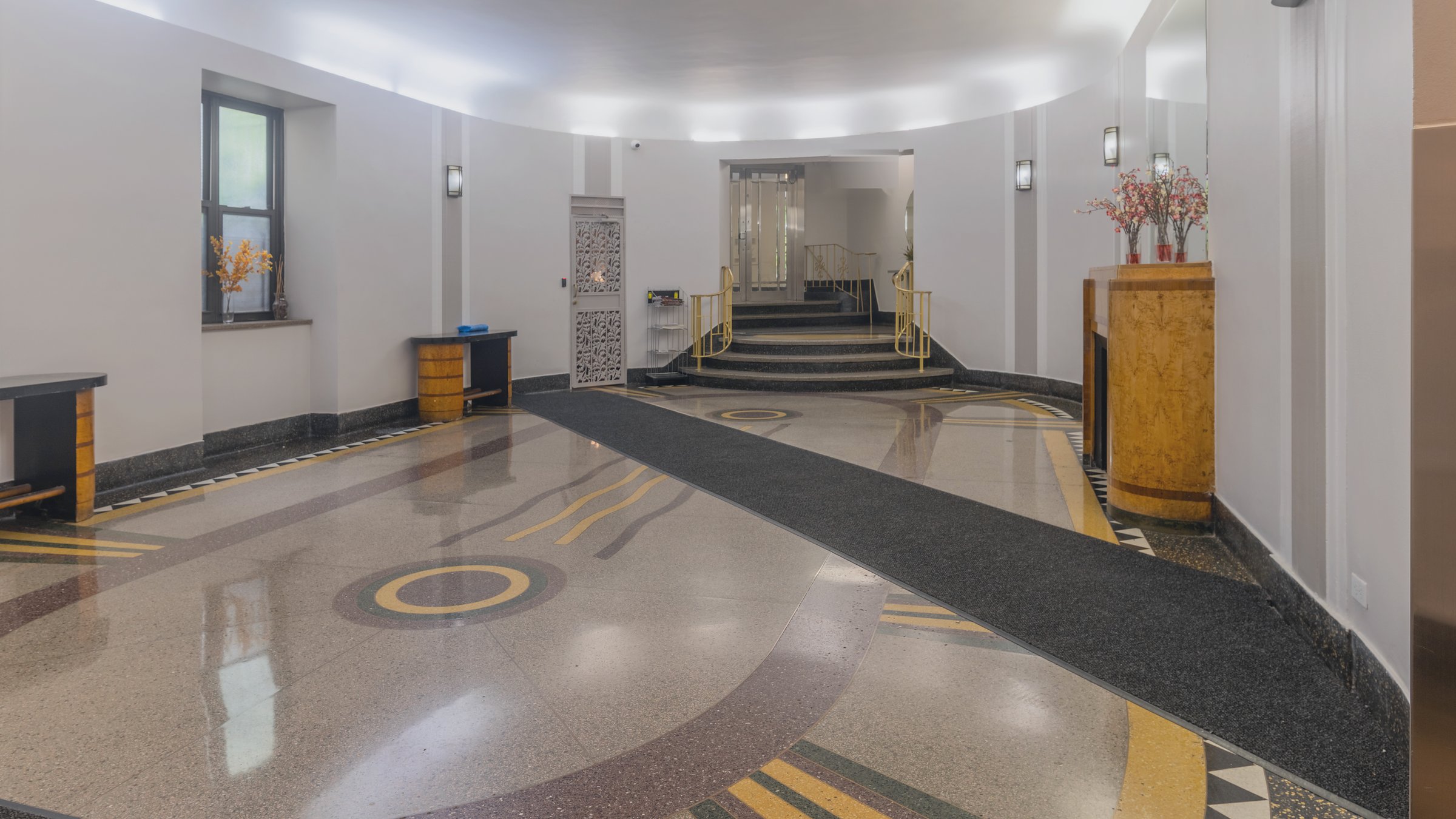 Daylight Art Deco lobby with patterned terrazzo floor, curved wall, and soft cove lighting