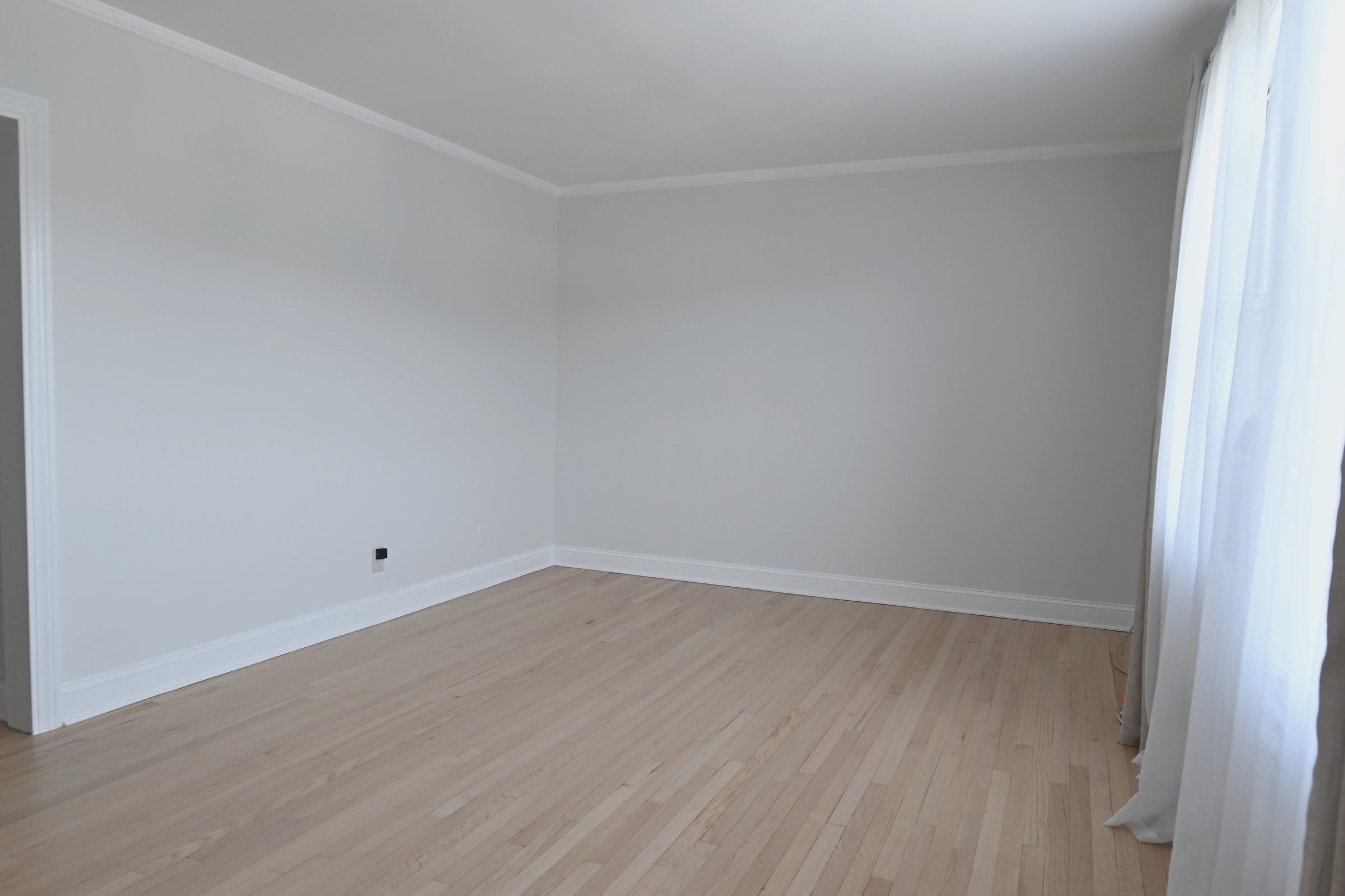 Soft empty room with light hardwood floors, neutral walls, and sheer curtains