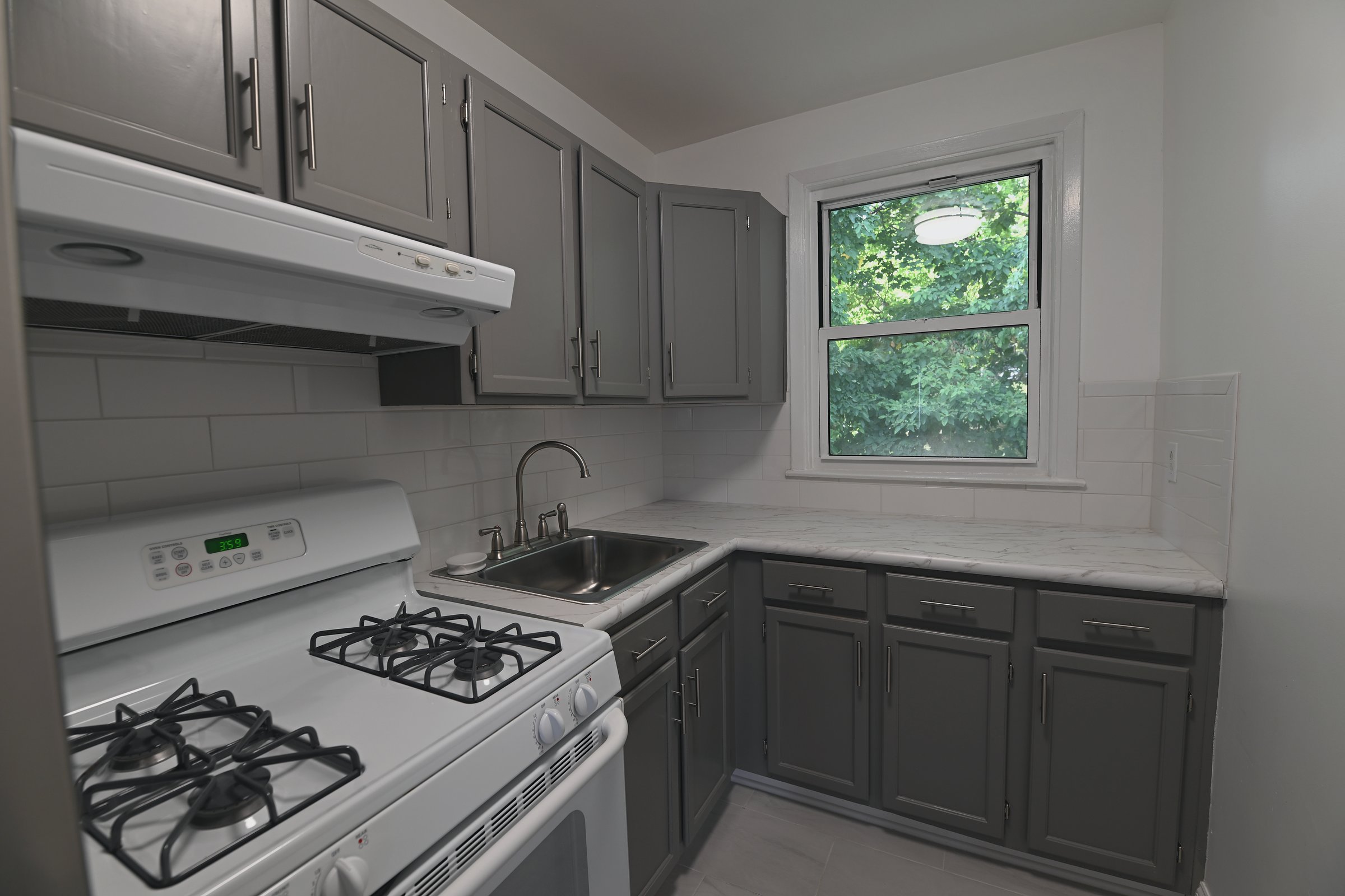 Bright kitchen with slate cabinets, white counters, subway tile, and a window over the sink